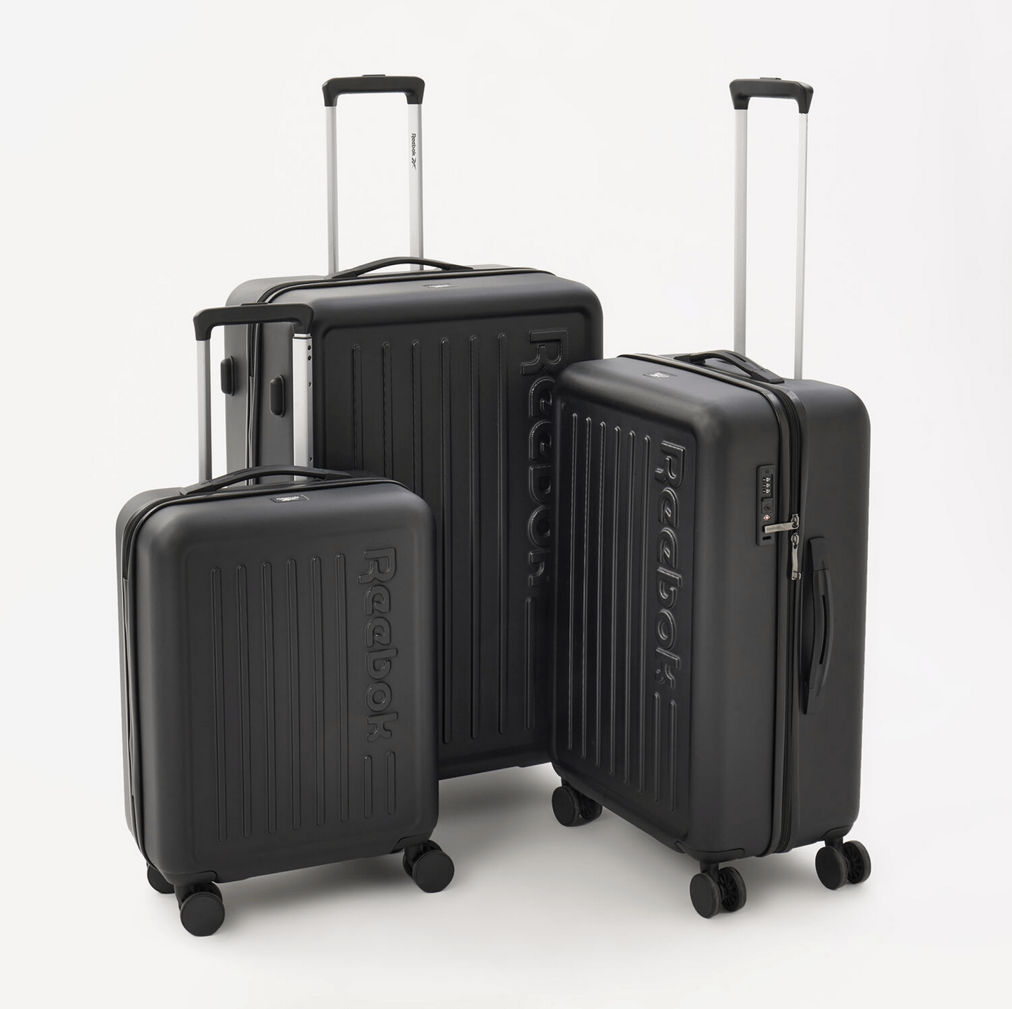 FCSI | An image of three black hard-shell suitcases of varying sizes arranged together. Each suitcase has "Reebok" embossed on its front and features a telescoping handle and four spinner wheels for easy mobility. The smallest suitcase is slightly in front of the other two.