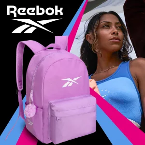FCSI | A woman in a blue tank top stands beside a large pink Reebok backpack with a pom-pom accessory. The background is black with blue and pink diagonal stripes and the Reebok logo prominently displayed.