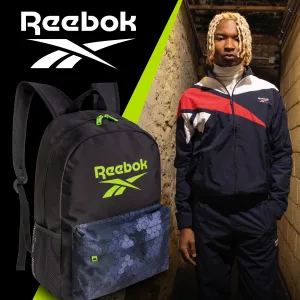 FCSI | A person with blonde hair wearing a navy and red Reebok tracksuit stands in a dimly lit hallway. To the left, there's a black Reebok backpack with a green logo and floral design. The Reebok logo is displayed above.