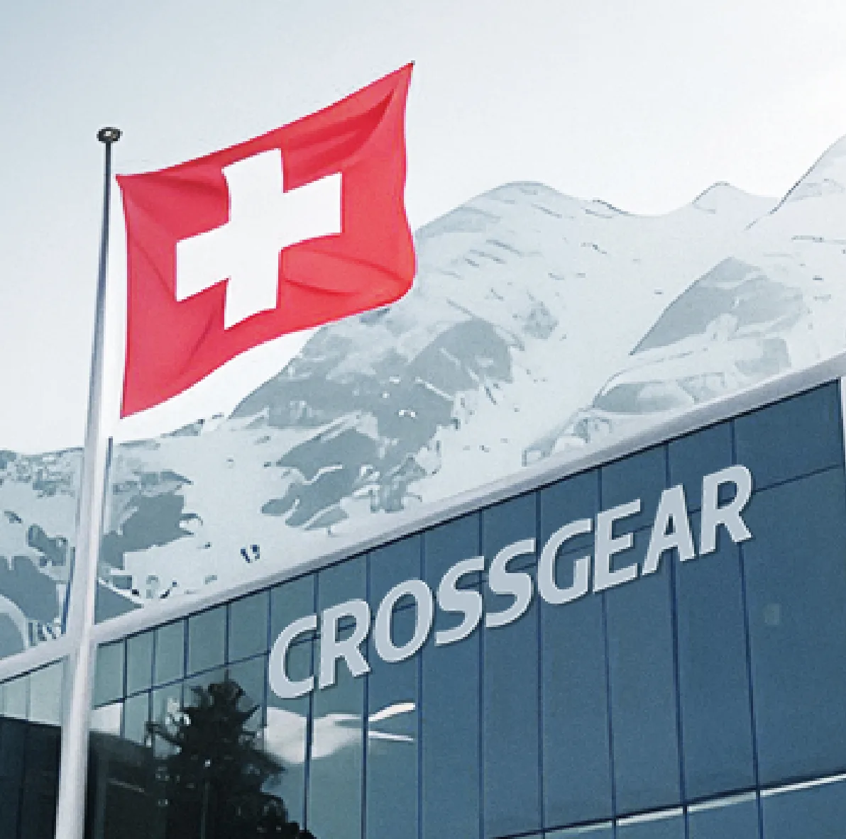 FCSI | A Swiss flag waves in front of a modern glass building with the word "CROSSGEAR" on it, set against a backdrop of snow-covered mountains.